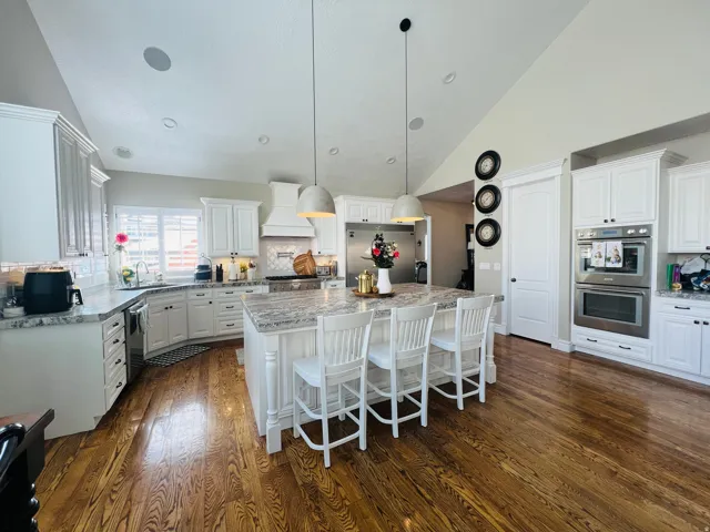 Kitchen featuring hardwood flooring, white cabinetry, granite countertops, a built-in double oven, and an island with pendant lighting