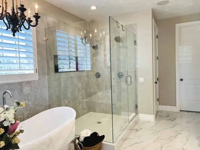 Freestanding soaking tub, glass-enclosed shower with tiled surround, plantation shutters, and recessed lighting