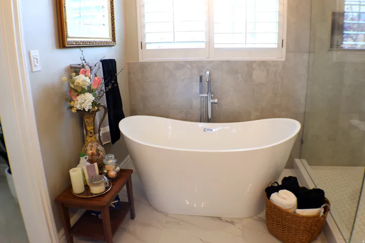 Freestanding soaking tub with polished chrome fixtures, surrounded by light-toned wall tile