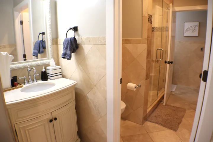 Vanity with a curved front and cabinet storage, under-mount sink with chrome faucet, large framed mirror, and a glass-enclosed shower with tile surround