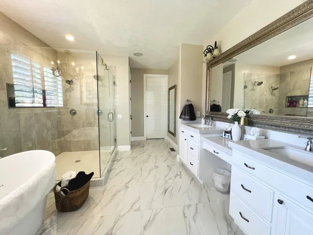 Spacious bathroom featuring a freestanding tub, expansive glass-enclosed shower with tiled walls, dual vanities with integrated sinks, and large-format tile flooring