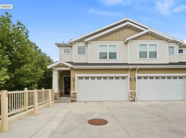 Two-story residence featuring light-toned siding, a multi-pane front door, two garage doors with window accents, and a concrete driveway