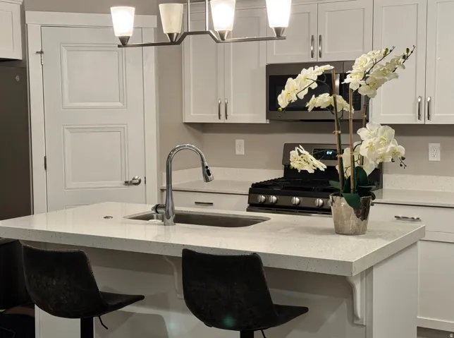 Kitchen island with integrated sink and chrome faucet, white shaker cabinetry, stainless steel microwave, and gas range