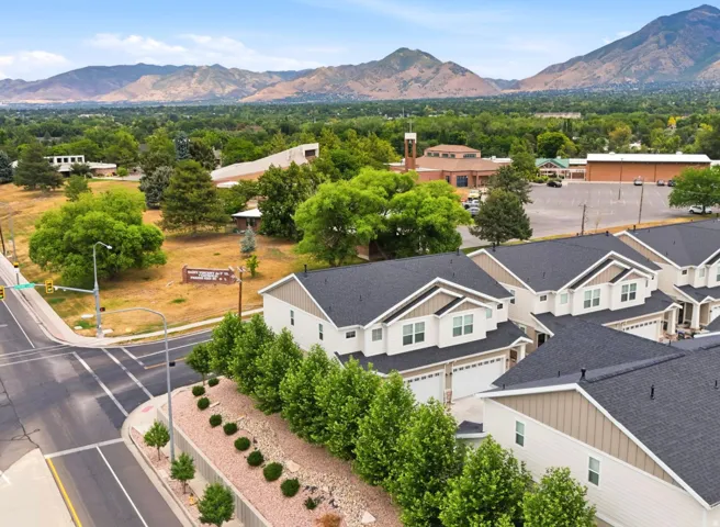 Contemporary townhome with a two-car garage, dark shingle roof, and light-colored siding, set against a backdrop of distant mountains and mature trees