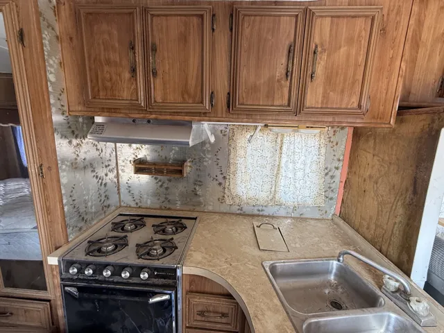 Built-in gas range with four burners, double basin sink, under-cabinet range hood, and wood-finish cabinetry