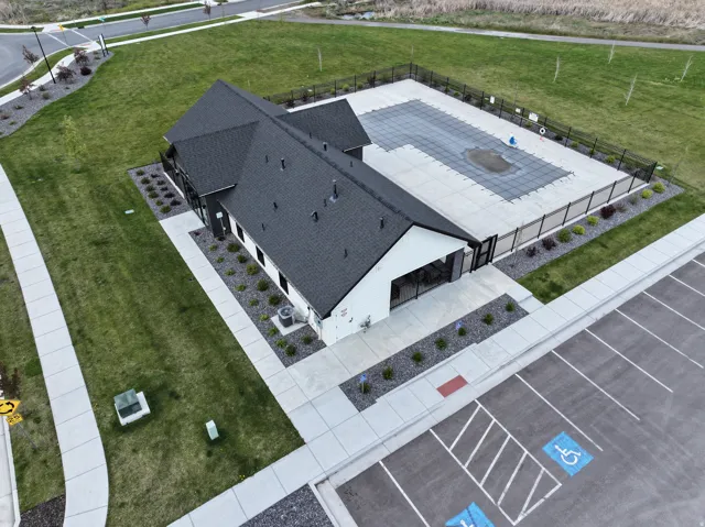 Contemporary building with a dark shingle roof, a fenced pool area, manicured landscaping with decorative rock, and a dedicated parking lot