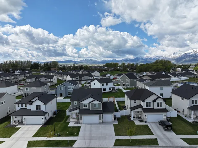 Residential neighborhood with a mountain backdrop, featuring modern homes with dark roofs, concrete driveways, and green lawns