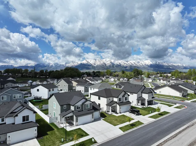 Expansive neighborhood with diverse residential structures, concrete driveways, and manicured lawns, set against a backdrop of snow-capped mountains