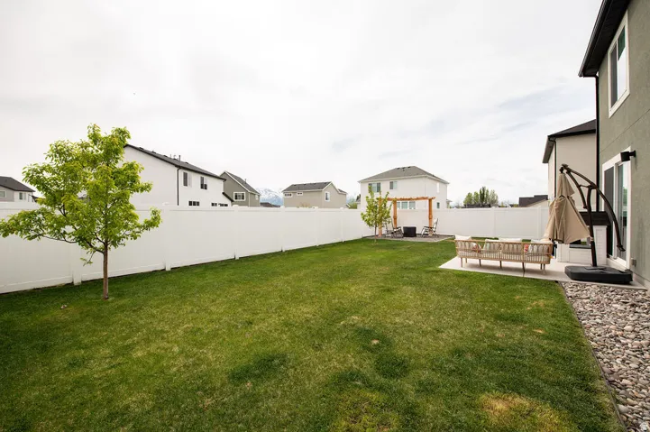 Expansive lawn area with a young tree, white privacy fencing, and a concrete patio