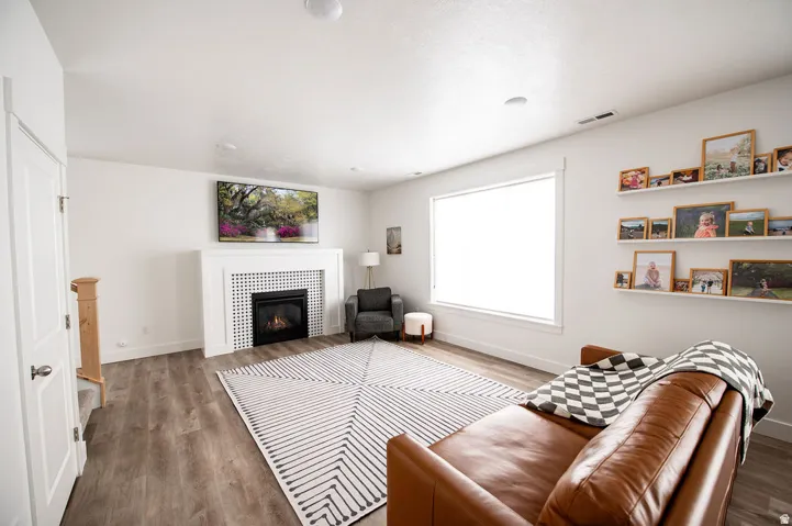 Living area featuring wood-finish flooring, a white mantel, and a fireplace with a tiled surround
