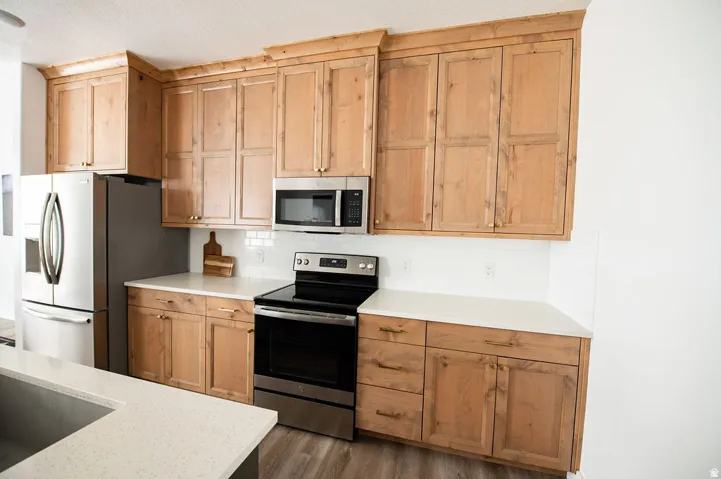 Light-finish wood cabinetry with gold-tone hardware, white countertops, stainless steel appliances, and white subway tile backsplash