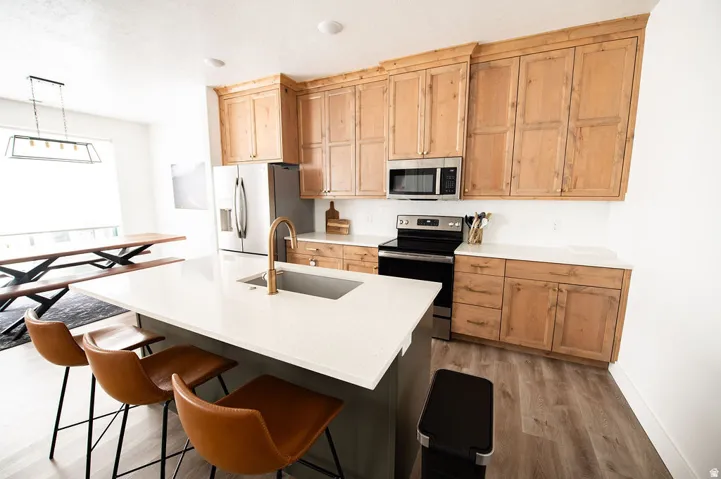 Kitchen featuring wood cabinetry, stainless steel appliances, white countertops, and wood-finish flooring