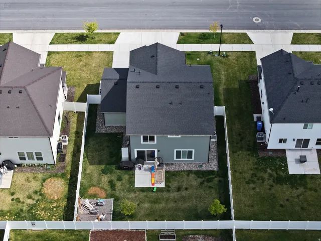 Vinyl fencing, rear patio, dark shingle roof, green siding, and manicured lawn