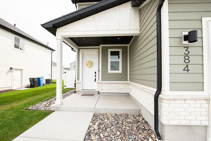 Exterior featuring light green siding, white brick detailing, a covered porch entry, and a contemporary wall light fixture