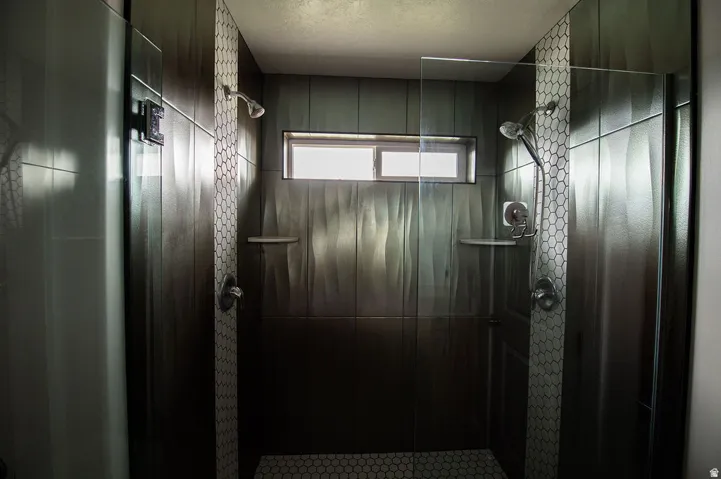 Spacious walk-in shower with dual shower heads, textured wall tile, transom window, and hexagonal floor tile