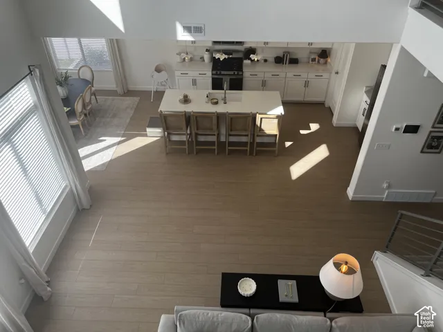 Open-concept living space featuring wood-finish flooring, a kitchen island with seating, white cabinetry, and large windows with blinds