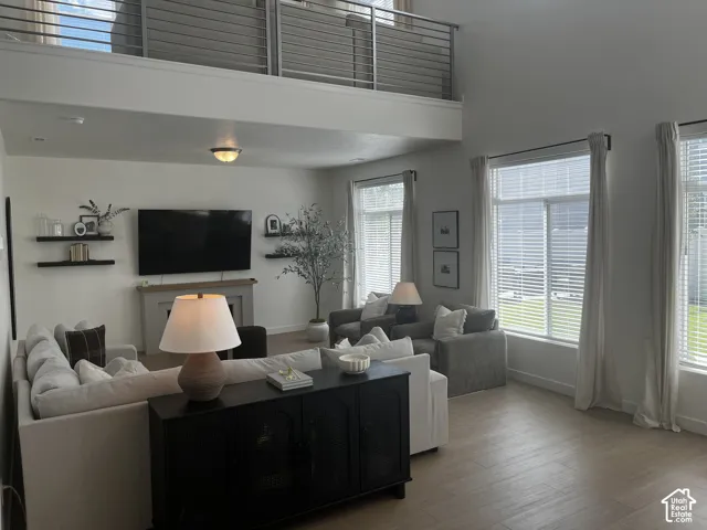 Two-story living area featuring a vaulted ceiling, wood-finish flooring, multiple windows, a decorative fireplace, and an upper-level railing