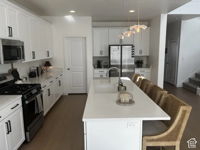 Modern kitchen featuring white cabinetry, stainless steel appliances, a center island with sink, quartz countertops, and wood-finish flooring