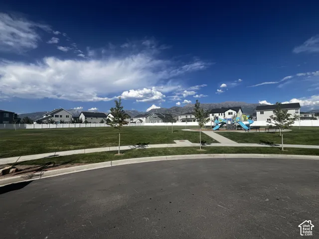 Expansive green space featuring a playground with slides and climbing structures, paved walking paths, and mature trees