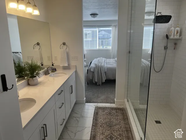 Double vanity with undermount sinks and light-toned countertops, large vanity mirror, white subway tile shower, clear glass shower enclosure, and white tile flooring