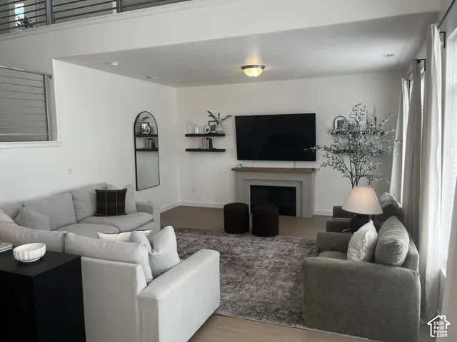 Spacious living area featuring light wood-finish flooring, a contemporary fireplace with a light-toned mantel, a built-in recessed television, and an upper-level overlook