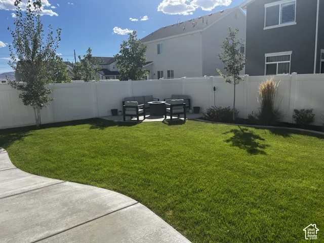 Expansive backyard with a manicured lawn, concrete patio, and white privacy fencing