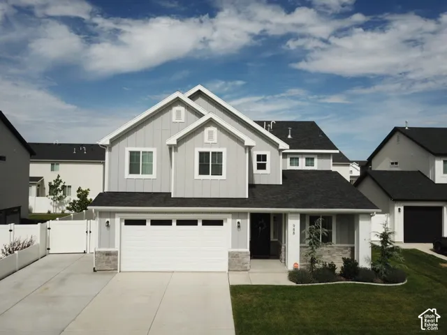 Two-story residence with a light gray facade, dark shingles, an attached two-car garage, manicured lawn, and a paved driveway