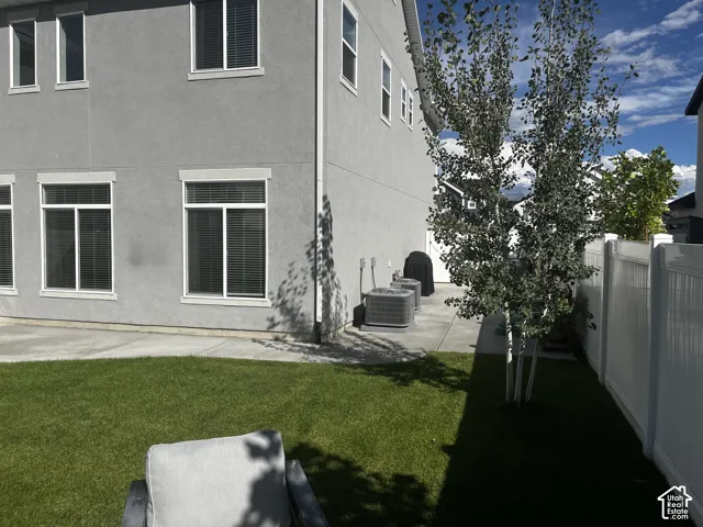 Manicured lawn with a white vinyl fence, mature trees, and a concrete patio