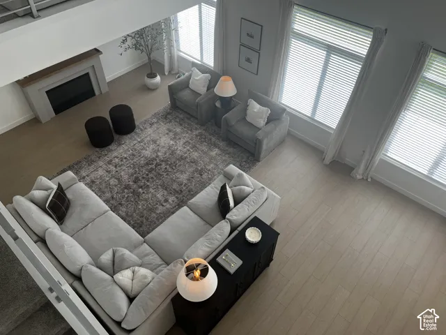 Spacious living area featuring a fireplace with a wood mantle, large windows with blinds, and light wood-finish flooring
