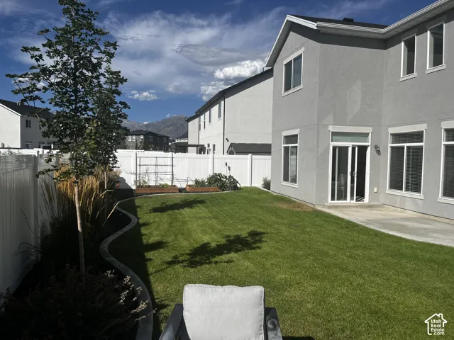 Expansive backyard featuring a manicured lawn, concrete patio, and white privacy fencing