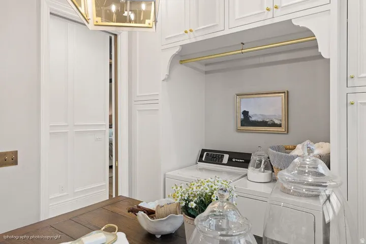 Built-in upper cabinetry with brass hardware, brass hanging rod, white paneled walls, and a recessed appliance area