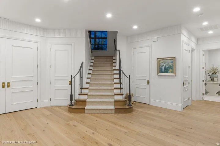 Light wood-finish flooring, a carpeted staircase with an iron railing, recessed lighting, and panel doors