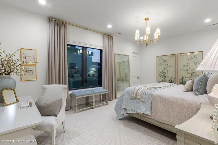 Recessed lighting, a brass chandelier, full-height window with drapery, light-toned carpeting, and a built-in vanity desk