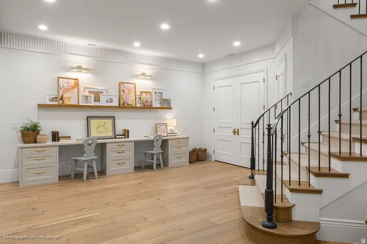 Light wood-finish flooring, built-in desk units with drawers, wall-mounted display shelf, and a staircase with an iron railing
