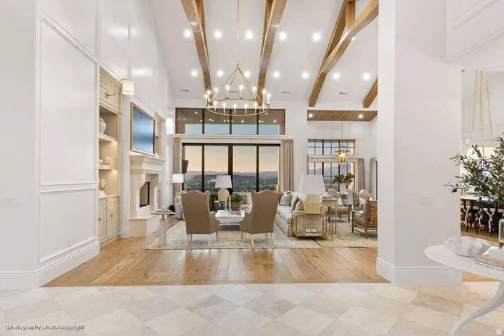 Vaulted ceilings with exposed wood beams, expansive floor-to-ceiling windows, built-in shelving with integrated lighting, and a prominent fireplace