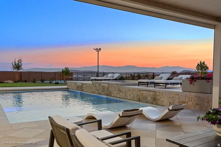 Outdoor living area featuring a rectangular swimming pool, stone-clad water feature, expansive tiled patio, and mountain scenery