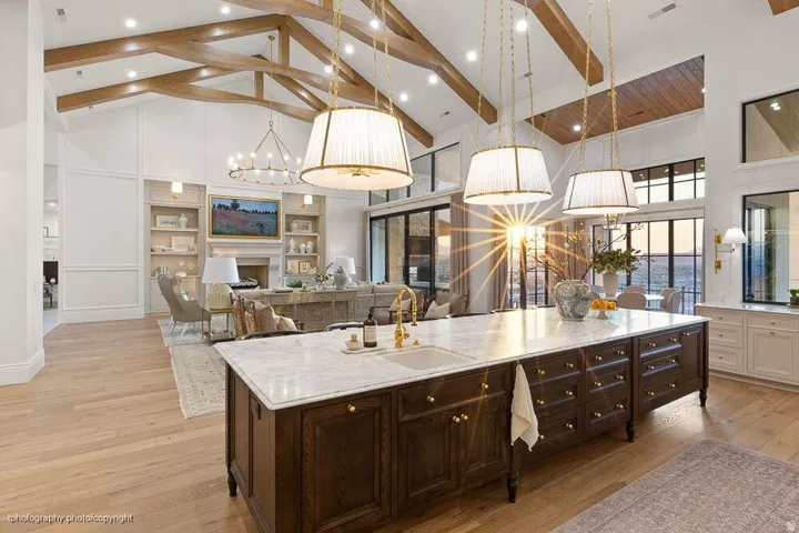 Vaulted ceilings with exposed wood beams, a spacious kitchen island with a stone countertop, built-in cabinetry, and large windows