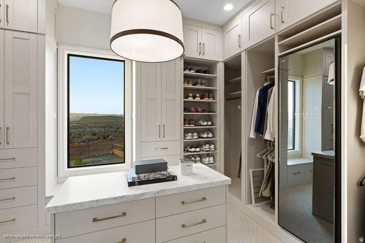 Custom built-in cabinetry, central island with a stone countertop, integrated shelving, and dedicated hanging storage