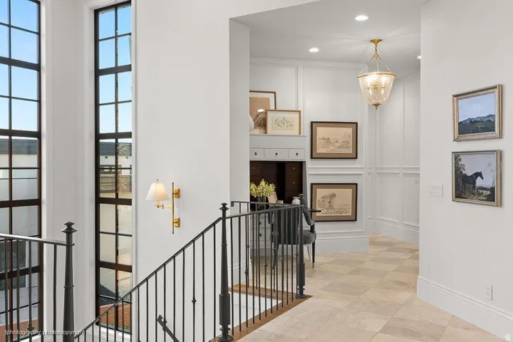 Tall multi-pane windows, black wrought iron railing, wall sconce lighting, coffered wall paneling, and checkered tile flooring