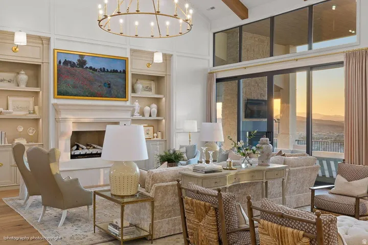 Vaulted ceiling with exposed wood beams, built-in shelving, fireplace with stone surround, large glass doors, and a decorative chandelier