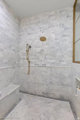 Full-height tile shower with a built-in bench, recessed niche, wall-mounted shower head, and handheld shower wand