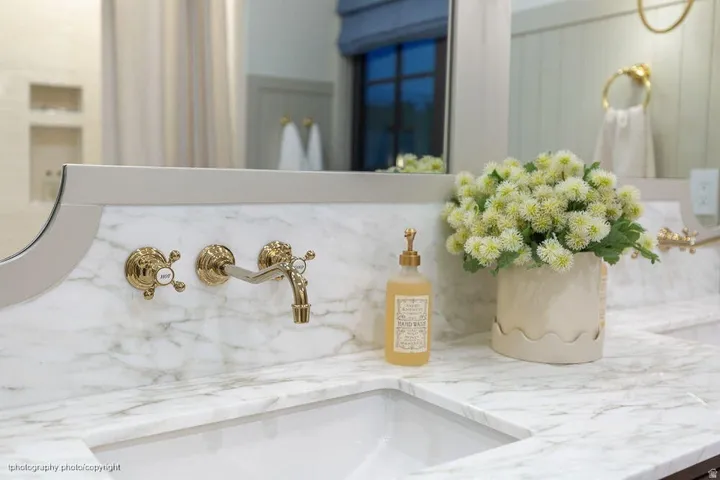 Integrated rectangular sink with a marble countertop, wall-mounted polished brass faucet, and an arched mirror