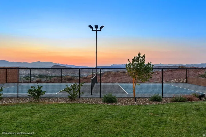 Private tennis court with a chain-link fence, surrounded by mature desert landscaping