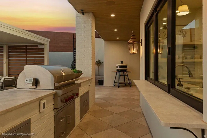 Outdoor kitchen with built-in stainless steel grill and pizza oven, light-toned stone countertops, and recessed lighting