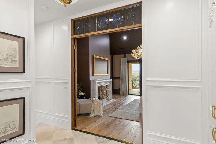 Paneled walls, ornate ceiling fixture, wood-finish flooring, decorative fireplace, and transom window with circular glass details