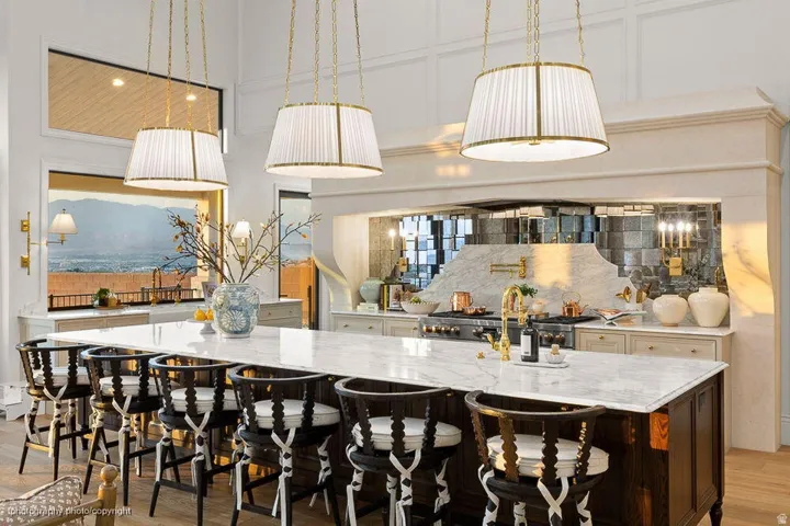 Kitchen island with a light-toned stone countertop, overhead pendant lighting, wood-finish flooring, and integrated range with mirrored backsplash