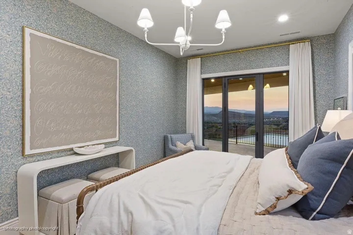 Patterned wall covering, a decorative wall sconce, recessed lighting, and a sliding glass door opening to an exterior balcony with a railing