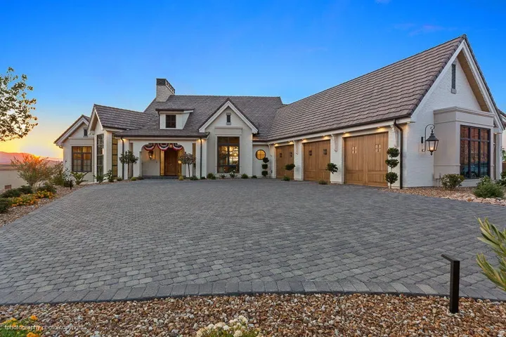 Paved driveway with a herringbone pattern, stucco exterior, multi-car garage with wood-finish doors, prominent bay window, and a gabled roofline