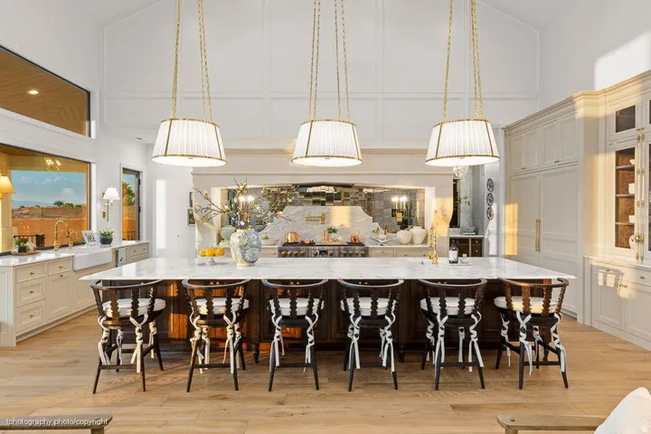 Kitchen featuring an expansive center island, a farmhouse sink, light wood-finish flooring, a vaulted ceiling with architectural detailing, and recessed panel cabinetry