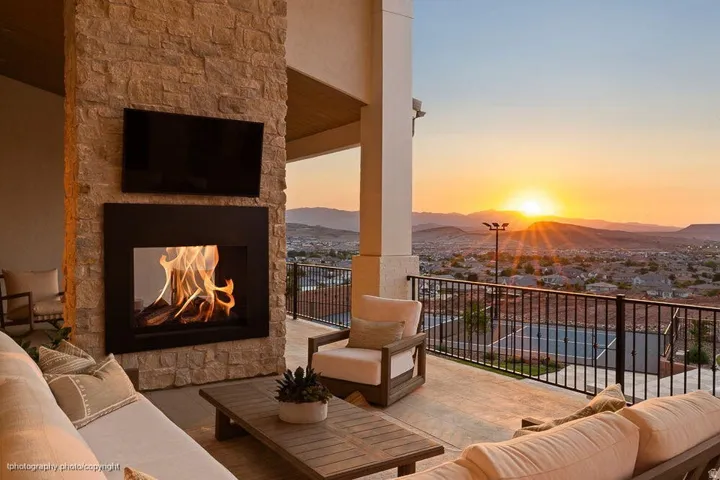 Stone-clad outdoor fireplace with integrated television, expansive concrete patio, and dark metal railing